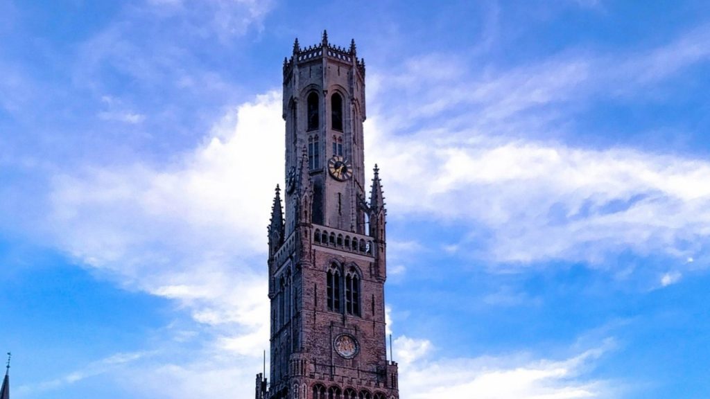 The iconic Belfry of Bruges (Belfort) standing tall against a bright blue sky, its Gothic architecture a testament to the city's rich history.