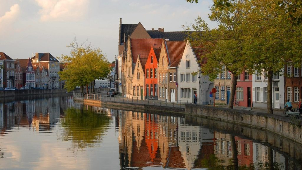 Colorful traditional houses reflecting in the tranquil canal waters of Bruges, with their distinctive façades creating a postcard-perfect scene.