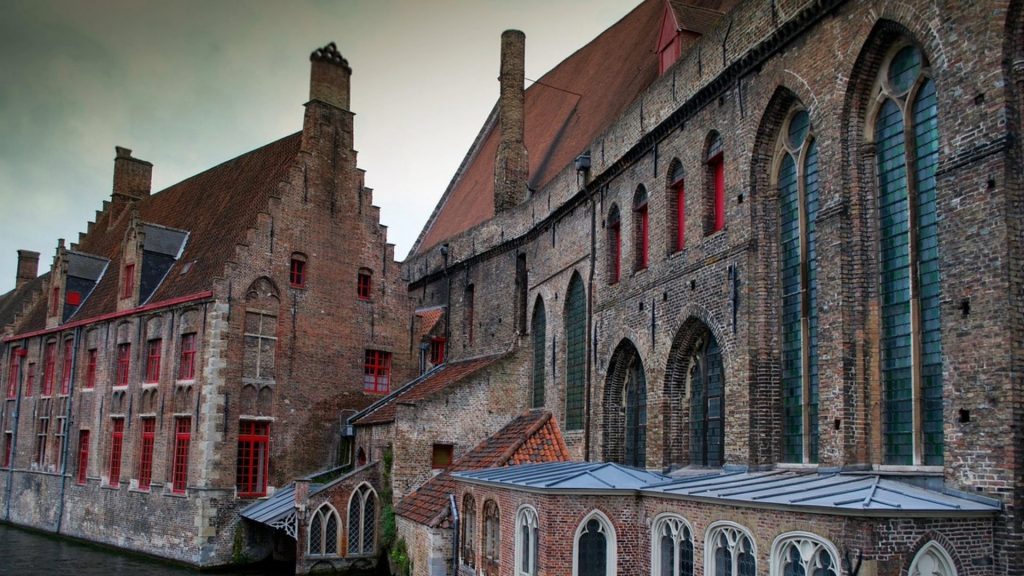 Historic brick buildings with distinctive step-gabled architecture alongside a canal in Bruges, showcasing the city's remarkably preserved medieval character.